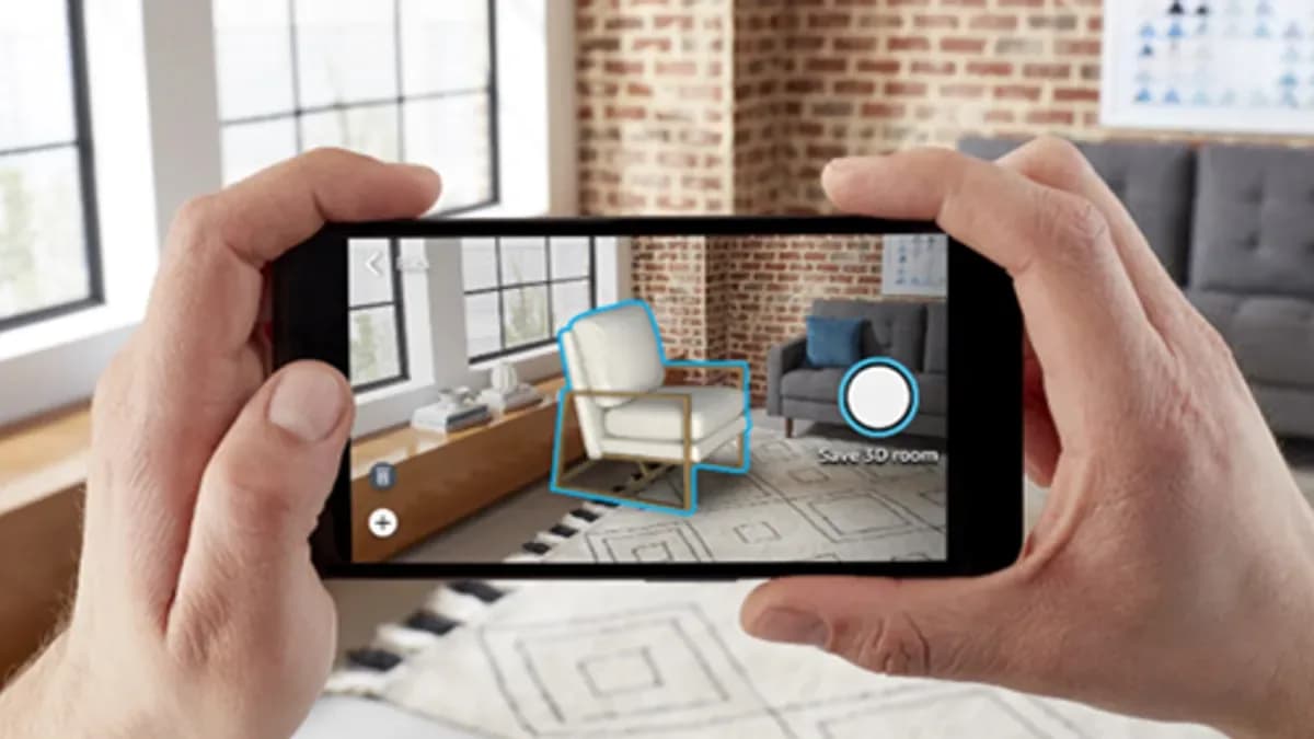 Hands holding a phone that places a white armchair into the shopper's living room through the camera, with a Save 3D room button on screen